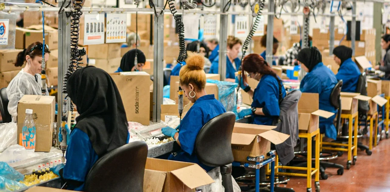 Suasana lantai produksi pabrik FMCG dengan banyak operator di lini assembly. Ilustrasi tanda sistem produksi tidak efisien.